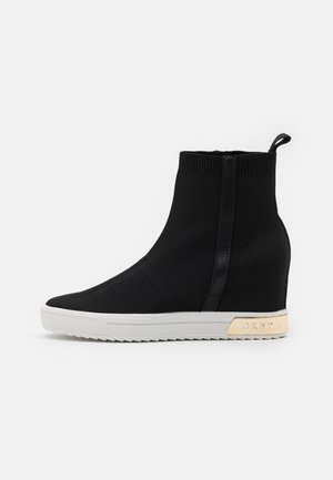 Czarne sneakersy na koturnie z białą podeszwą, prążkowanym mankietem wokół kostki, pętelką do ściągania i złotym logo DKNY na pięcie.