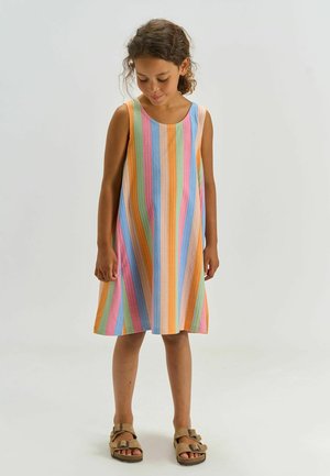 Girl wearing a sleeveless, knee-length dress with vertical pastel stripes and brown sandals, standing against a plain light background.