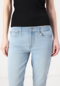 Jeans de mezclilla azul claro con un diseño clásico de cinco bolsillos, que presentan un cierre de botón dorado y sutiles detalles de costura.