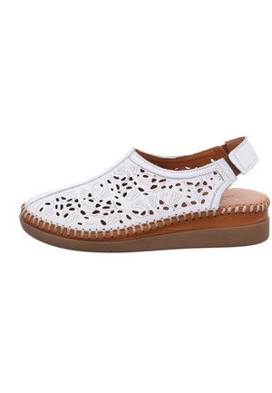 White leather slingback shoe with floral cut-out patterns, stitched brown sole, and adjustable Velcro strap.
