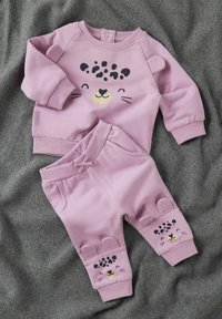 Conjunto de sudadera y pantalones rosas hecho de un tejido suave. Presenta un diseño de cara de leopardo en la parte superior y acentos a juego en los puños de los pantalones.