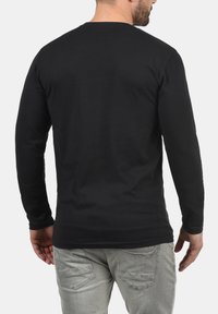 Schwarzes Langarm-T-Shirt mit Rundhalsausschnitt, aus einem weichen, glatten Stoff gefertigt. Nahtdetails am Saum und an den Ärmeln.