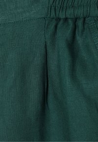 Gros plan d’un tissu vert foncé montrant une ceinture élastique froncée et une texture finement tissée.