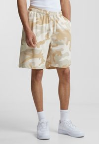 Beige camouflage shorts with an elastic waistband and drawstring. Made of soft fabric, featuring a regular fit and side pockets.