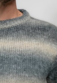 Suéter de punto con cuello redondo, en tonos degradados de gris y crema; mezcla de lana texturizada con puntadas visibles y acabado suave.