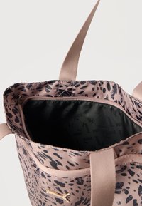 Ροζ και μαύρη τσάντα ώμου με βούλες, με μπεζ λαβές, με μερικώς ανοιχτό φερμουάρ που αποκαλύπτει μαύρη εσωτερική επένδυση με λογότυπα Puma.