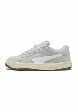 Jasnoszare zamszowe buty sportowe Puma z białym paskiem, beżową midsolem, brązową podeszwą zewnętrzną i sznurowadłami, widoczne z boku na białym tle.