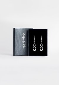 Silverörhängen i en svart sammetslåda. Designen har överlappande cirkulära former med en polerad finish. Lådan har en strukturerad grå yta.