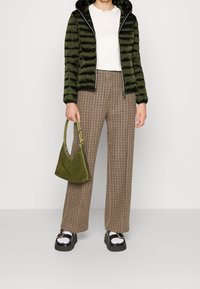 Groene pufferjas, witte shirt, bruine houndstooth wijde broek, groene suède tas, stevige zwarte schoenen met zilveren accenten.