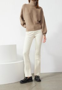 Beige coltrui met een geribbeld textuur, gecombineerd met off-white flare jeans en zwarte leren instappers met een gespsluiting.