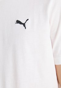 Hvit t-skjorte med korte ermer laget av myk bomull, har en svart brodert logo av en hoppende katt på venstre bryst.