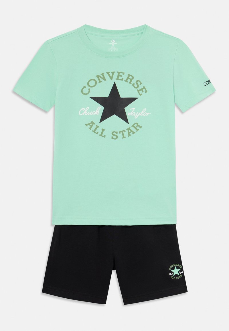 Camiseta de algodón verde menta con gráfico de estrella negra y texto "Converse All Star", combinada con pantalones cortos negros que presentan un logo verde en la pierna.