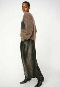 Bruin donzig sweater met een donkergrijze streep, gecombineerd met een zwarte leren rok en puntige zwarte enkellaarzen, die tactiele texturen laten zien.
