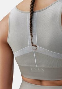 Crop top sportivo grigio chiaro realizzato in tessuto testurizzato, con cuciture bianche a contrasto e un logo sul retro, abbinato a un dettaglio di capelli intrecciati.