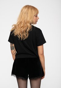 Black cropped t-shirt made of soft cotton, paired with black velvet shorts featuring lace trim. Model is viewed from the back.