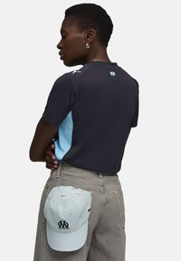 Marinblå och ljusblå atletisk polo med kort ärm, med logodetalj och en ljusblå keps med logotyp som ligger på bakfickan.