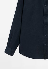 Navy blue long-sleeve shirt with a textured fabric, button-down front, and a curved hem. Features matching buttons and tailored cuffs.