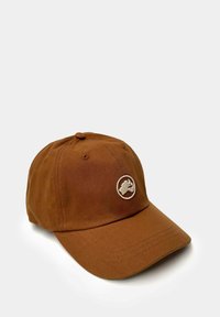 Gorra marrón hecha de un tejido texturizado con un ala curvada, que presenta un logo bordado beige en la parte frontal y ojales para ventilación.