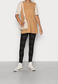 Beige ribbelstrick Oversized-Top, schwarze und karierte Slim-Fit-Hosen, weiße High-Top-Sneaker und eine hellfarbige, strukturierte Handtasche.