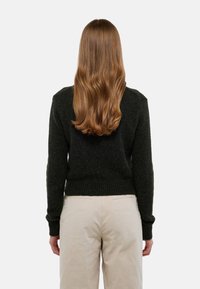 Pull en tricot vert foncé avec un col rond et des poignets côtelés, associé à un pantalon beige, visible de dos. Texture douce.