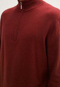 Roter, schließbarer Pullover mit hohem Kragen, aus weichem Strickstoff gefertigt. Verfügt über einen Viertel-Reißverschluss und eine glatte Textur.
