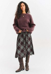 Bordowy, miękki sweter z szerokimi rękawami połączony z długą, kraciastą spódnicą w ciemnych odcieniach brązów i zieleni, uzupełniony jasnobrązowymi botkami za kostkę.