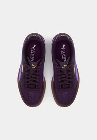 Fialové semišové tenisky s texturovaným povrchem, s jemným fialovým akcentem a hnědou gumovou podrážkou. Zlatý logo detail na boku.