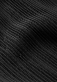 Primo piano di un tessuto nero a coste che mostra sottili linee verticali e pieghe delicate, creando texture e profondità.