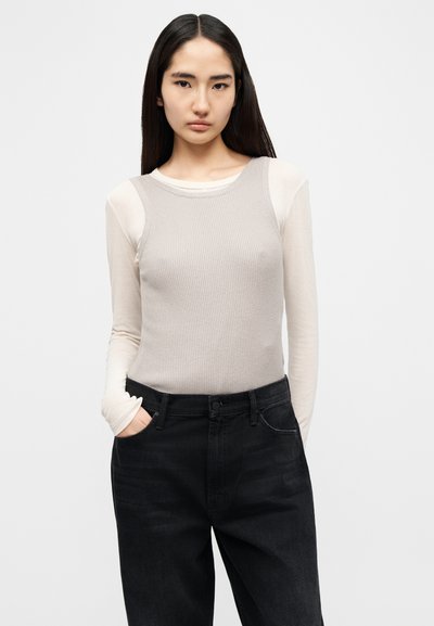 Ανοιχτό γκρι ριγωτό τοπ με μακριά μανίκια, φορεμένο πάνω από ένα κρεμ βασικό στρώμα, συνδυασμένο με μαύρο τζιν. Απλός σχεδιασμός με εφαρμοστή σιλουέτα.