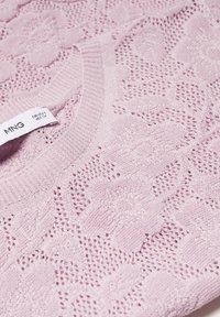 Lichtroze gebreide trui met een bloemenkantpatroon en een geribbelde halslijn. Zichtbaar label met daarop "MNG" en maatinformatie.