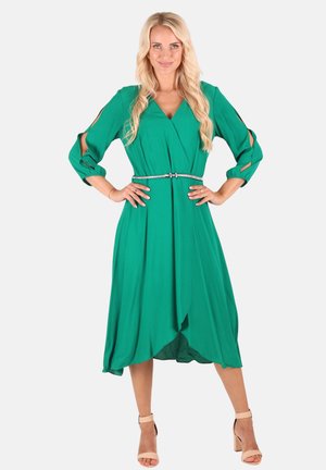 Grünes Kleid mit langen Ärmeln, V-Ausschnitt und Ausschnitten an den Schultern; verfügt über einen Bindegürtel und einen geschwungenen Saum.