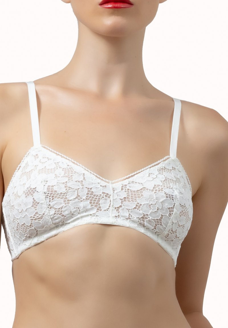 Donna che indossa un bralette bianco in pizzo floreale con spalline sottili, che mostra la parte superiore del torso e labbra rosse su sfondo bianco.