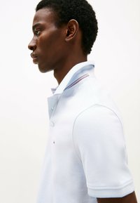 Polo shirt azzurro chiaro con tessuto testurizzato, colletto con bottoni e strisce a contrasto all'interno del colletto. Logo semplice sul petto.