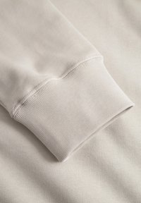 Beige sweatshirt fabric close-up, featuring a smooth texture and ribbed cuff detail, with visible stitching and soft stretch.