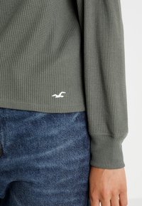 Grå ribbad långärmad topp med en subtil vit logotyp på f ållen, i kombination med blå denimjeans. Mjuk textur och snugga mudd.