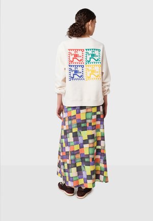 Crème sweatshirt met kleurrijke geometrische ontwerpen op de achterkant. Gecombineerd met een multi-kleurige geruite maxi rok en donkere schoenen.