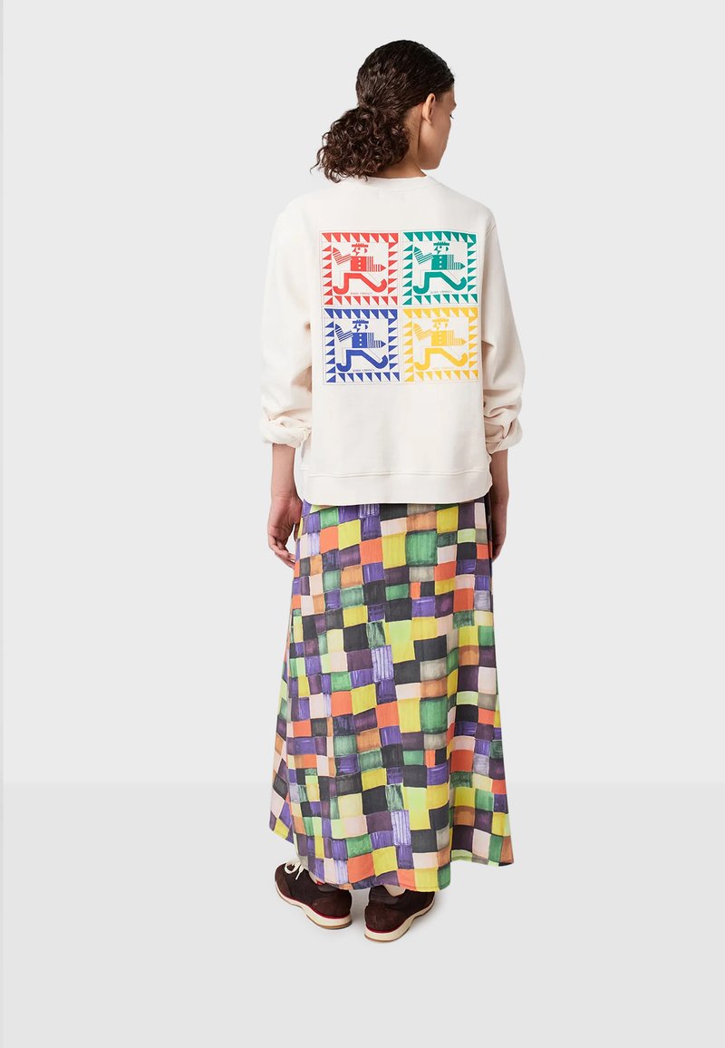 Felpa crema con design geometrici colorati sul retro. Abbinata a una maxi gonna a scacchi multicolore e scarpe scure.