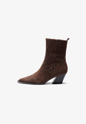 Bottines en suède marron avec un bout pointu, embellies de clous en argent dans un motif décoratif, et un talon empilé pour la stabilité.