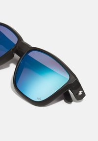 Juodos saulės akinių su stačiakampiais rėmeliais, turinčiais mėlynus gradientinius lęšius. Tekstūruoti šonų akcentai ir logotipo detalė ant šventinių.