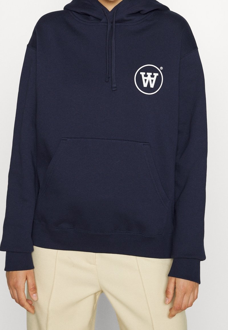 Mörkblå hoodtröja i mjukt tyg, med en känguruficka och en vit logotyp i cirkulär design på bröstet.