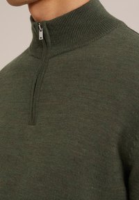 Suéter de cuello alto de cremallera en un verde oscuro, con canalé fino y una textura suave, que presenta un detalle de cremallera plateada.