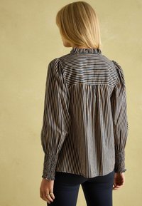 Striped blouse with elastic cuffs, featuring navy and cream vertical stripes. Soft fabric with a gathered back design and ruffled neckline.
