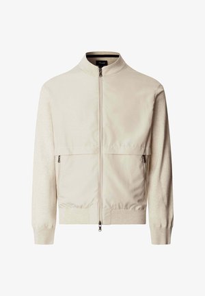 Beige jas met rits, met geribbelde kraag, manchetten en zoom, voorzien van twee voorzakken met rits en een glad stoffen paneel op de borst.