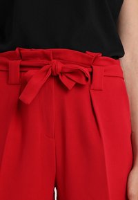 High-waisted red pants with fabric belt tied in a bow, paired with a black tucked-in top, showing waist to mid-thigh area.