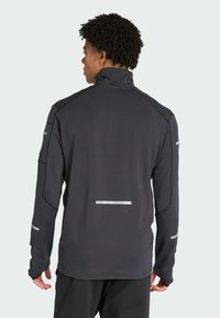Veste noire à manches longues avec col haut, tissu texturé, bandes réfléchissantes sur les manches et le dos, et design ajusté.