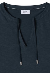 Encolure de chemise bleu foncé avec découpe en V et cordons, avec une étiquette de marque blanche "CECIL" à l'intérieur du col.