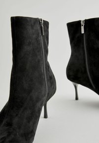Schwarze Wildleder-Ankle-Boots mit einem eleganten Design, seitlichen Reißverschlüssen und schmalen Absätzen, die eine glatte Textur und einen minimalistischen Stil präsentieren.