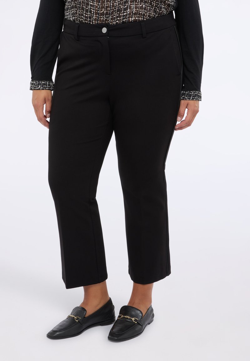 Černé kalhoty na míru se rovnými nohavicemi, navržené s hladkým povrchem a detaily předních kapes. Nosí se s černými mokasíny a vzorovanou košilí.