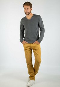 Grå v-neck sweater, lange ærmer, blød tekstur; sennepsfarvede bukser, slim fit, fem-lomme design; parret med hvide sneakers.