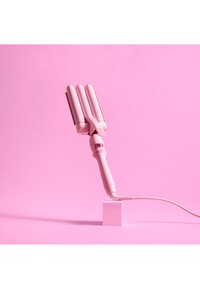 Fer à friser rose à triple baril avec une poignée texturée, un écran numérique et un cordon enroulé, reposant sur un piédestal blanc contre un fond rose.